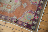 Distressed vintage Oushak rug corner with terracotta field and violet starburst border.