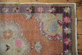 Distressed Oushak rug detail: terracotta field, purple starburst border, blush florals, and fringe.