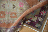 Rolled vintage Oushak rug showcasing distressed pile, terracotta, purple, and pink floral motifs.