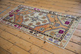Distressed Oushak rug close-up: pale orange field, fuchsia floral motifs, connecting purple vinery.