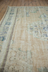 Distressed Oushak rug detail, worn beige pile, visible foundation, faded navy floral motifs.