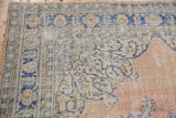 Distressed vintage Oushak rug corner showing blue rococo borders and worn pale sandalwood field.