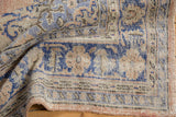 Folded corner of vintage distressed Oushak carpet with worn pile, blue, and sandalwood rococo motifs.