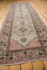 Distressed Oushak runner with repeating floral medallions, geometric borders in mauve, beige, coffee brown.