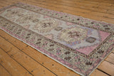 Distressed Oushak runner with mauve, violet, and coffee brown starburst and meandering vine border.