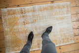 A person's view of a distressed vintage Oushak rug, showing its low-pile, worn texture for scale.