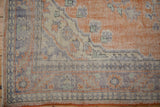 Distressed vintage Oushak corner with worn pile, featuring faded terracotta, blue, and ivory vinery.