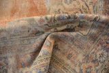 Close-up of folded distressed Oushak carpet pile showing rust, sky blue, and ivory tones.
