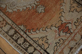 Distressed vintage Oushak rug corner, showing wear, geometric border, dusty rust, and beige.