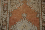 Textured distressed Oushak rug field in abrashed dusty rust with patterned beige border.