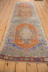 Distressed orange, blue, and sand field of a vintage Oushak runner with stylized motifs.