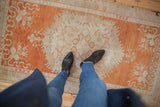 Distressed vintage Oushak rug in faded tangerine, ivory, and pale slate, with floral patterns and even wear.