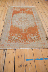 Corner of distressed vintage Oushak rug with faded tangerine field, ivory blossom leaf border, and fringe.