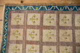 Distressed Oushak rug with beige panels, simplified yellow motifs, brown grid, and teal vine border.