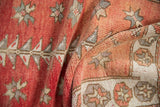 Distressed Oushak rug fold, showing faded cinnabar, ivory, starbursts, and pomegranate border motifs.