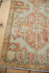 Distressed vintage Oushak rug corner with worn brick red ram's horn motif, saffron hints, and fringe.