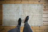 Vintage distressed Oushak rug displaying worn pile, ivory, beige tones, and faint patterns.