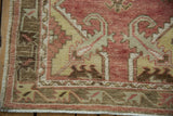 Distressed Oushak rug corner with faded red, saffron, brown motifs, and visible fringe.
