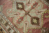 Distressed Oushak rug texture showing faded brick red and coffee brown scrolling leaves.
