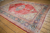 Close-up: Distressed vintage Oushak rug texture, showing worn cherry red and navy geometric patterns.