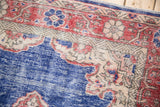Distressed Oushak rug detail: cobalt blue field meets faded rust spandrel, showing mostly even wear.