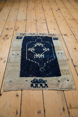 Distressed Oushak mat corner showing ivory stepped border, navy field, and fringe.