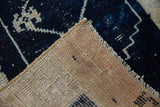 Detail of distressed Oushak rug, showing navy blue pile, exposed knot heads, and beige foundation.
