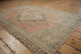 Distressed Oushak rug corner showing muted rose and beige field with intricate borders.