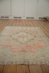 Distressed Oushak rug corner showing faded rose, blush, and beige border motifs.