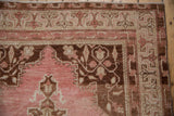 Distressed Oushak rug corner, featuring blush floral palmettes and coffee brown arabesques.