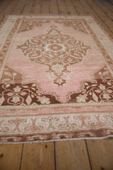 Distressed vintage Oushak rug corner showing blush field, coffee brown floral spandrel and border.