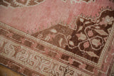 Distressed vintage Oushak rug corner showing faded blush field, coffee brown floral spandrel, and border details.