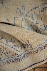 Vintage Oushak rug close-up showing worn ivory pile and faded blue wave motifs.