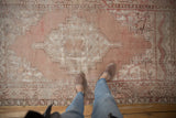 Distressed Turkish Oushak rug, stepped medallion, floral motifs, dusty mauve, ivory, exposed foundation.