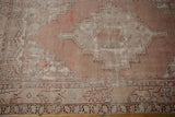 Distressed vintage Oushak rug detail showing worn foundation, dusty mauve, and ivory serrated motifs.