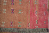 Distressed Oushak runner detail: dusty blush, pink fields, geometric motifs, green checkered border.