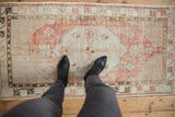 Distressed Oushak runner, showing faded cinnabar red and ivory pattern and texture underfoot.