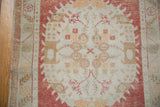 Distressed vintage Oushak rug close-up: cinnabar red floral border and ivory field with wear.