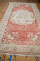 Distressed vintage Oushak rug showing pale cinnabar field and ivory floral main border.