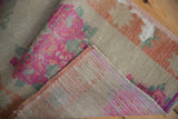 Folded distressed Oushak rug pile, faded pink floral pattern, visible foundation, and selvage.