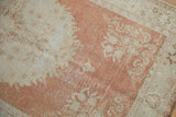Textured distressed pile of vintage Oushak rug with faded cinnabar red and ivory floral patterns.