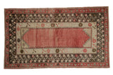 Distressed Oushak rug with faded raspberry field, ivory spandrels, and dark floral vine borders.