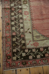 Distressed Oushak rug corner with faded raspberry field, stepped spandrel, charcoal vine border.