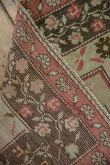 Folded distressed Oushak rug reveals faded raspberry border, delicate vine motif, and woven foundation.