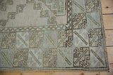 Distressed Melas rug corner, geometric lattice, serrated border, and soft seafoam green tones.