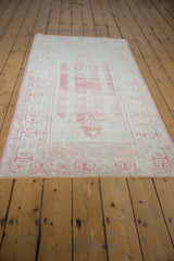 Distressed Oushak rug runner end, showing pale pink ram's horn border and ivory fringe.