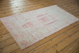 Distressed pink and ivory Turkish Oushak rug corner with intact side cord selvage.
