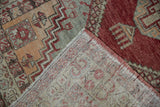 Distressed Oushak rug pile with red and sage tones, showing hand-knotted beige foundation.