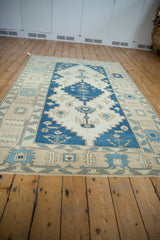 Vintage distressed Oushak rug: indigo blue stepped medallion with serrated leaf motifs on ivory field.