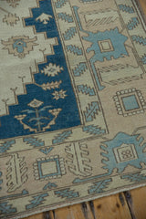 Distressed Oushak rug showing indigo blue field, beige vinery, serrated leaves, and geometric motifs.